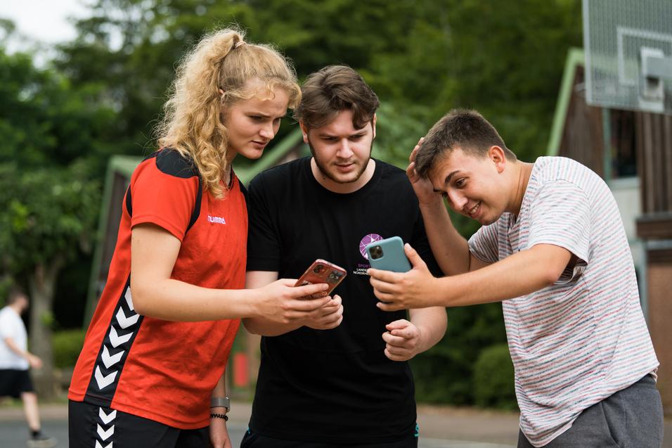 Drei Jugendliche stehen zusammen und schauen auf ihre Smartphones, um etwas anzusehen oder zu besprechen.